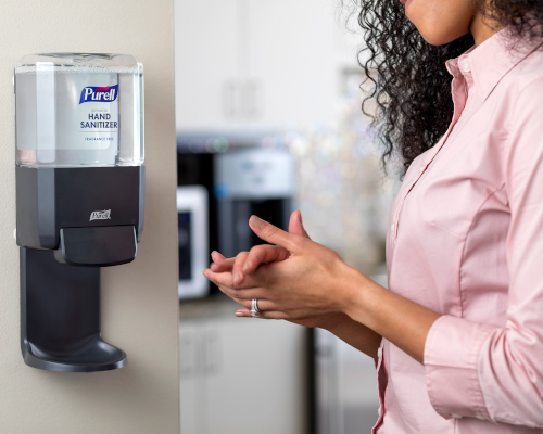 Hand sanitizer wall unit with person applying sanitizer solution to hand.